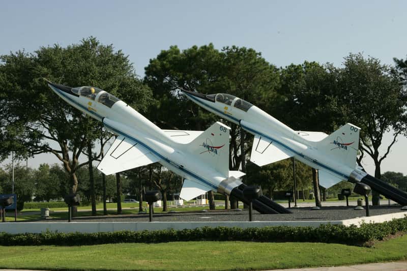 Two jet aircraft on display at an outdoor exhibit, positioned nose-up, surrounded by trees and greenery.