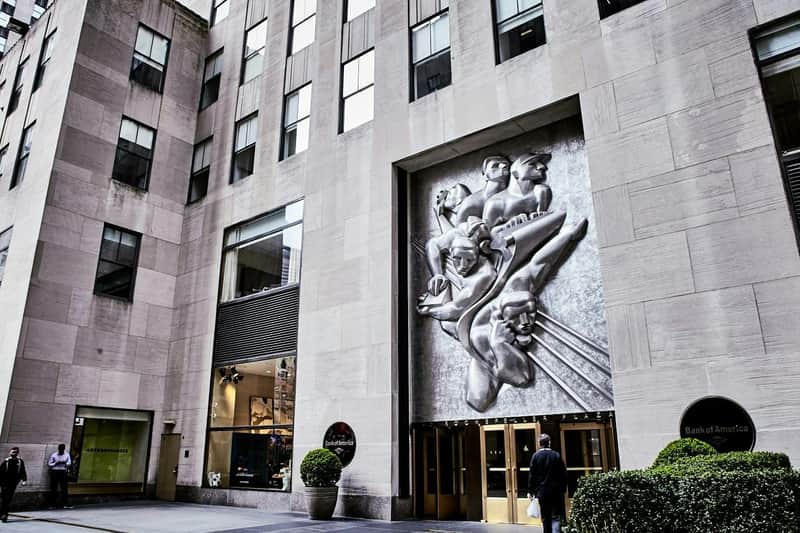 Rockefeller Center City Cards & Passes (New York) Large stone building with high windows, a metal relief sculpture, entrance doors labeled "Rockefeller Plaza," and Bank of America signage.