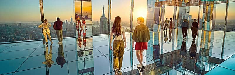 SUMMIT One Vanderbilt City Card (New York) People stand and walk on a mirrored observation deck with a view of a city skyline at sunset.