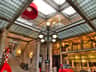Interior of a vintage building with a glass ceiling, ornate railing, central lamp post, stairs, and a red car display near a gallery.