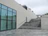 Modern building with large windows on the left and wide stone steps leading up to the right, surrounded by gray paving stones.