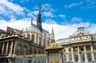 Historic Gothic cathedral and palace with ornate gold gate under a blue sky with scattered clouds.