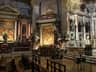 Lavishly decorated church interior with large paintings, gold accents, statues, and wooden pews on a checkered floor.