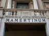 A stone entrance with a balustrade above it, featuring the text "PRIGIONE DEI SS APOSTOLI PIETRO E PAOLO MAMERTINUM."