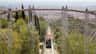 Un funiculaire rouge gravissant une pente raide à travers une colline verdoyante, avec un paysage urbain et l'océan en arrière-plan.