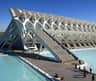 Modern white building with an intricate design, adjacent to reflective pools of water; people walking and gathering nearby.