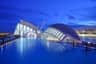 Modern futuristic buildings with white structures and large glass windows, surrounded by a reflecting pool under a twilight sky.