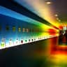 A long hallway with numbered shelves displaying glass containers filled with colored liquids, illuminated by vibrant, colorful lighting.