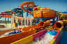 People splashing down colorful water slides on inflatable tubes at an outdoor water park under a clear blue sky.