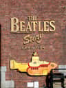 Signa en una paret de maons amb "The Beatles Story Exhibition" i una il·lustració submarina pintada de groc.