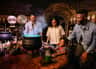 A family of four smiles around a bubbling cauldron in a dimly lit room filled with potion bottles and laboratory equipment.