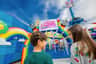 Two children are smiling at each other in front of "Unikitty's Disco Drop" ride entrance with colorful rainbows and vibrant decor.