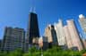 A skyline with various high-rise buildings against a clear blue sky, with trees in the foreground.