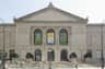 The facade of the Art Institute of Chicago, featuring banners for a Van Gogh exhibit, flags, and people walking by.
