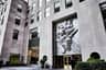 Rockefeller Center City Cards & Passes (New York) Large stone building with high windows, a metal relief sculpture, entrance doors labeled "Rockefeller Plaza," and Bank of America signage.