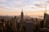 Top of the Rock City Cards & Passes (New York) View of a city skyline at sunset, dominated by tall skyscrapers, with a river and distant buildings in the background.