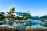 Un parc aquatique tropical avec un grand toboggan bleu sinueux, des palmiers, des rochers et une piscine sous un ciel bleu clair.
