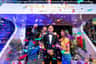 Three people celebrate with confetti and drinks around a wax figure in a tuxedo at Madame Tussauds Orlando.