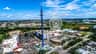Aerial view of an amusement park with a tall swing ride, Ferris wheel, parking lots, buildings, and surrounding greenery under a blue sky.
